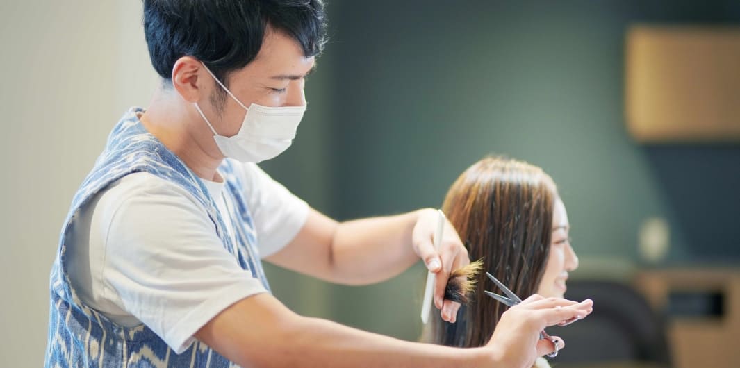 男性店員が女性客の髪の毛を切ろうとしている写真